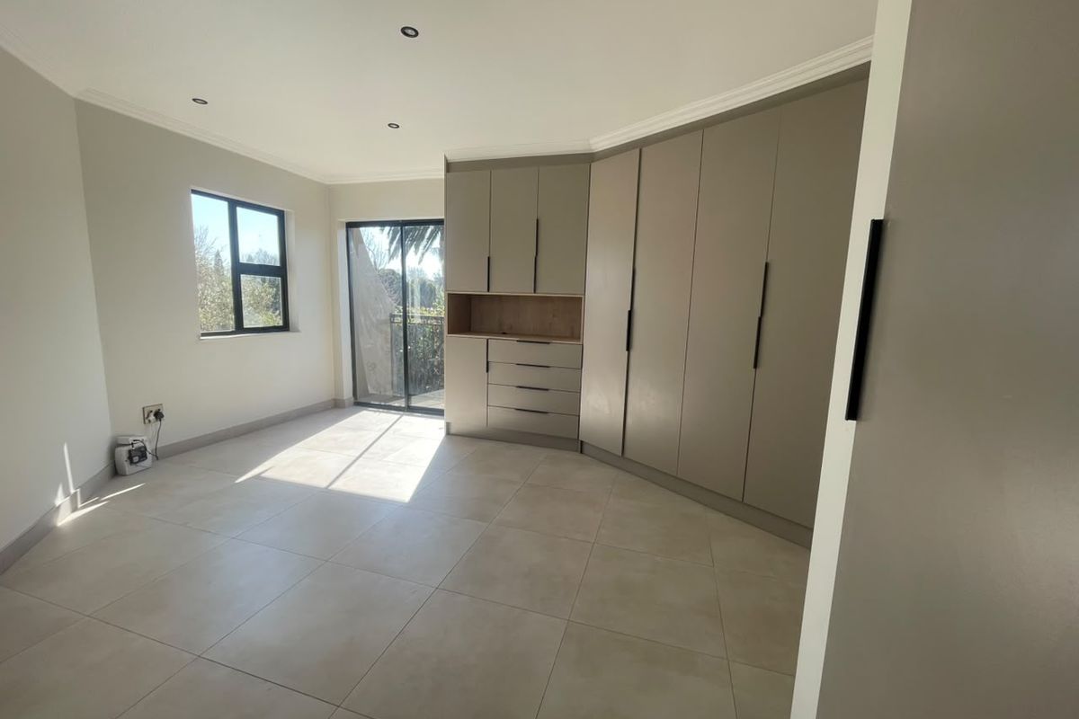 A bright, modern bedroom featuring neutral tiled flooring, extensive built-in cabinetry, and a sliding door providing access to an outdoor area.
