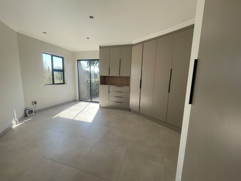 A bright, modern bedroom featuring neutral tiled flooring, extensive built-in cabinetry, and a sliding door providing access to an outdoor area.