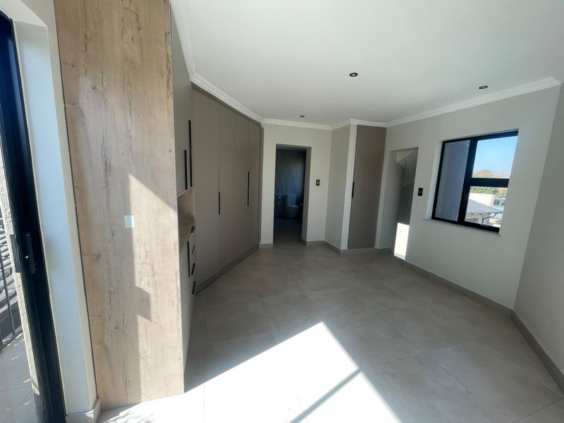 A spacious, modern bedroom featuring neutral tiled flooring, extensive built-in cabinetry, recessed lighting, and large windows allowing for ample natural light.