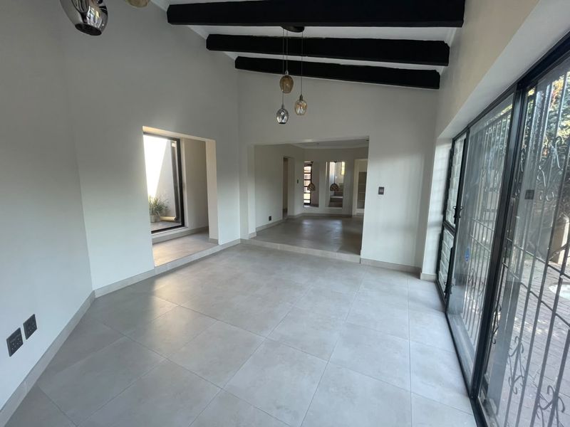 Spacious, light-filled living area featuring modern tiled floors, exposed ceiling beams, and large sliding glass doors leading to the exterior.