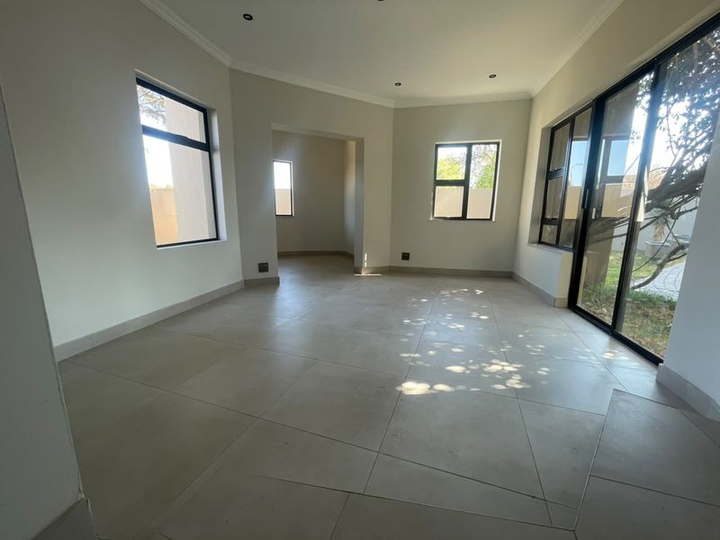 A bright, empty living area featuring large aluminium sliding doors, tiled flooring, and recessed downlighting, offering a clean and neutral space.