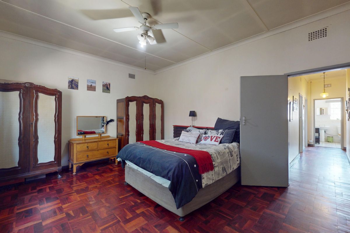 Spacious bedroom featuring traditional parquet flooring, a ceiling fan, and direct access to an adjoining hallway.