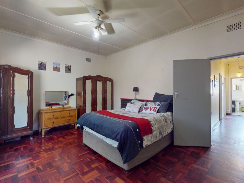 Spacious bedroom featuring traditional parquet flooring, a ceiling fan, and direct access to an adjoining hallway.
