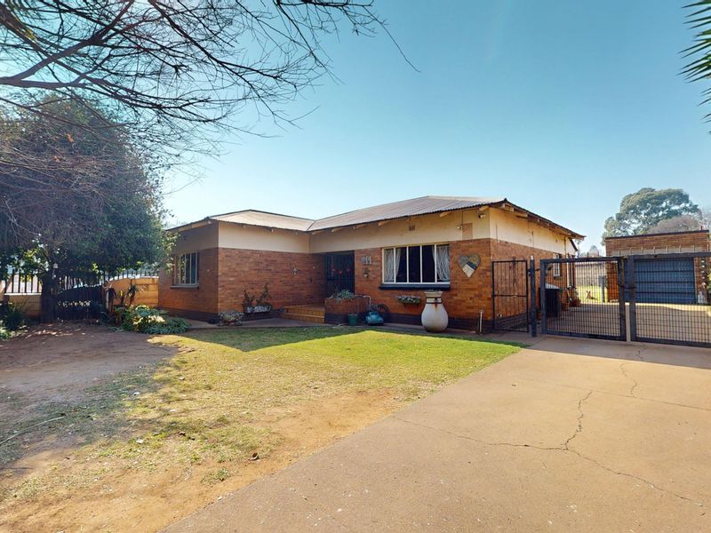 Front view of a single-story brick house featuring a metal roof, gated driveway, and a detached garage on a spacious residential lot.