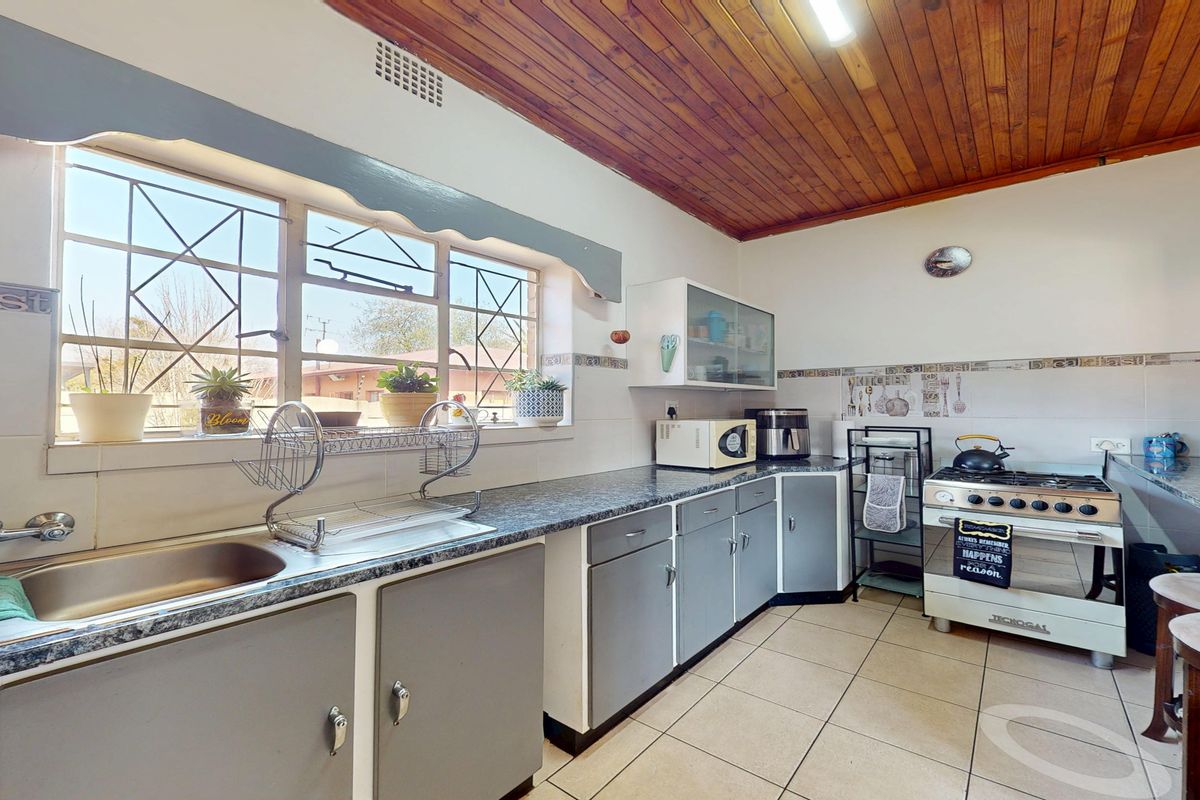 Functional kitchen featuring laminate countertops, a stainless steel sink, a freestanding gas stove, and a distinctive timber ceiling with tiled flooring.