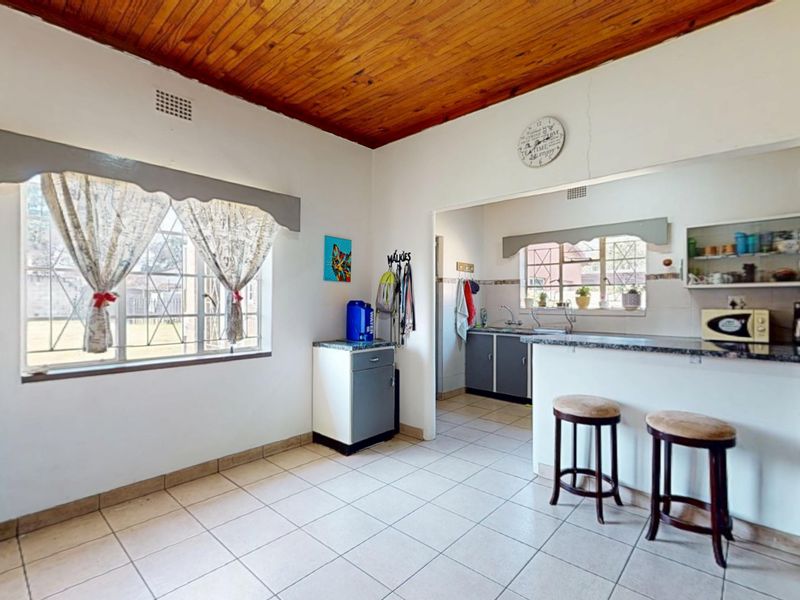 Open plan kitchen and dining area featuring a timber ceiling, tiled floors, granite breakfast bar, and built-in cabinetry with security bars on windows.