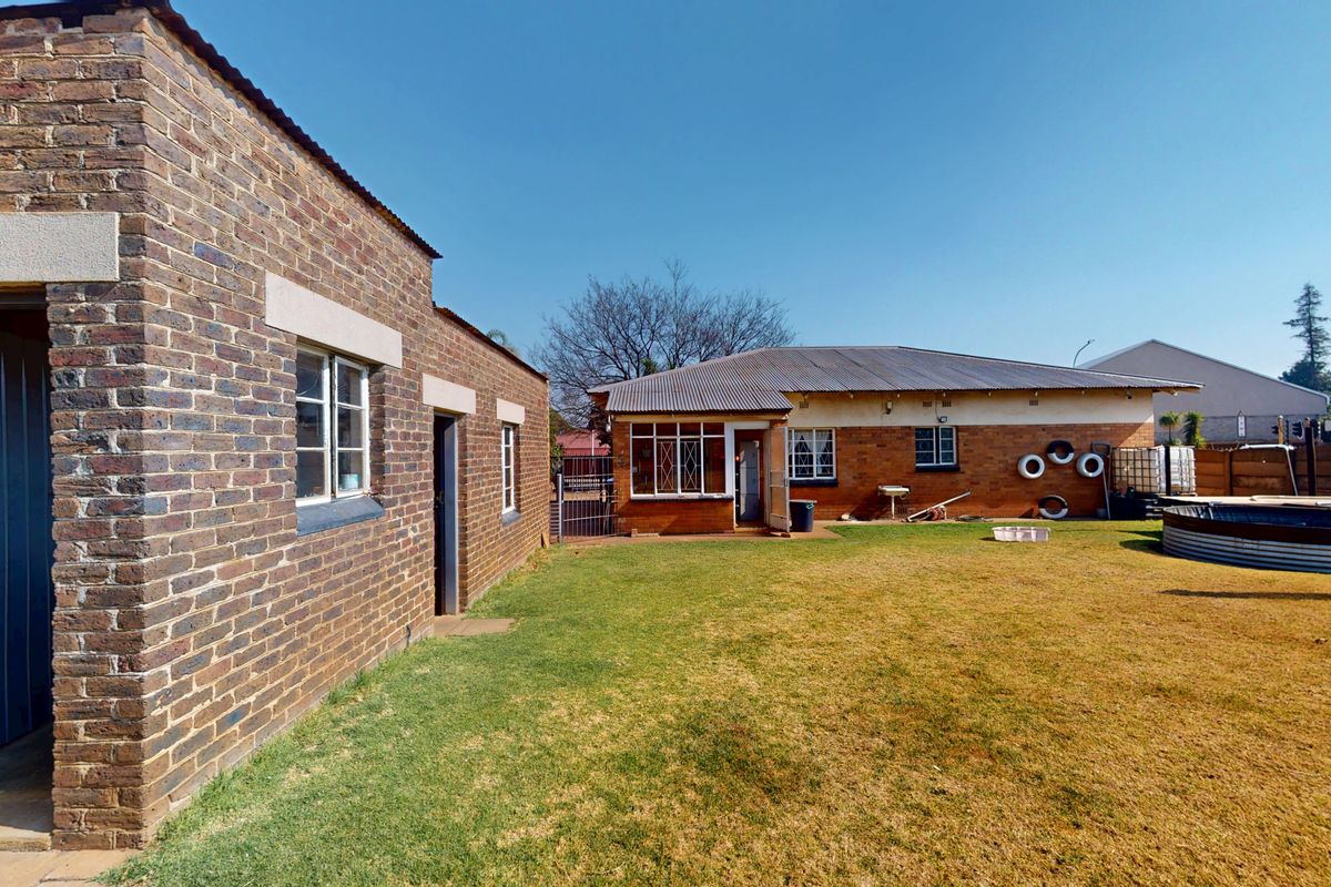 Rear view of the property featuring face brick construction, corrugated metal roofing, steel window frames, and a spacious backyard with an above-ground water tank.