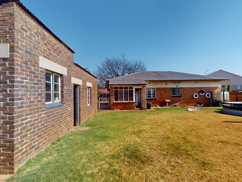 Rear view of the property featuring face brick construction, corrugated metal roofing, steel window frames, and a spacious backyard with an above-ground water tank.