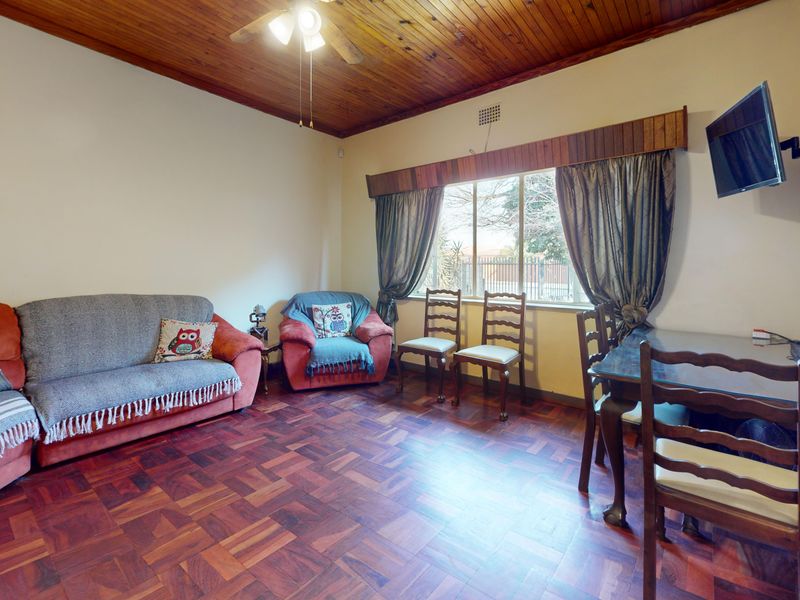 A living room featuring traditional parquet flooring and a timber-paneled ceiling, offering a classic layout with natural light from the window.