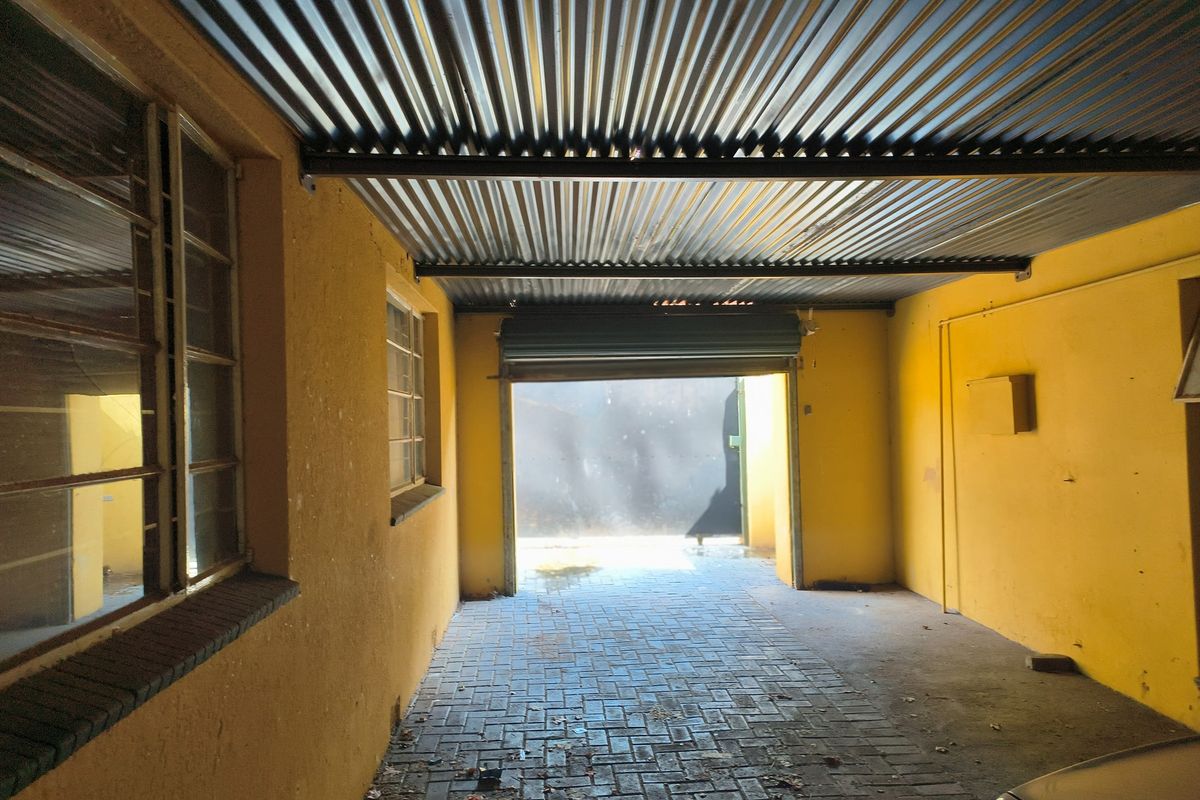 A functional garage space featuring a corrugated metal roof, paved flooring, and a roller shutter door, requiring some maintenance and cosmetic updates.