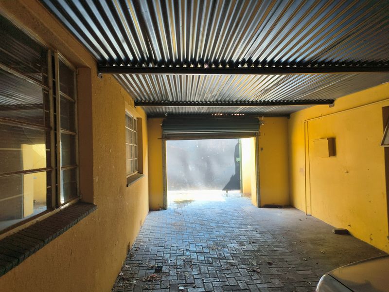A functional garage space featuring a corrugated metal roof, paved flooring, and a roller shutter door, requiring some maintenance and cosmetic updates.