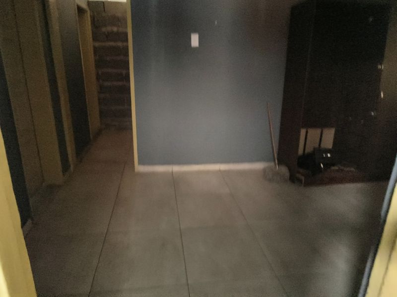 A dimly lit, empty hallway featuring tiled flooring and plain wall finishes, requiring cosmetic updates to improve the overall aesthetic.