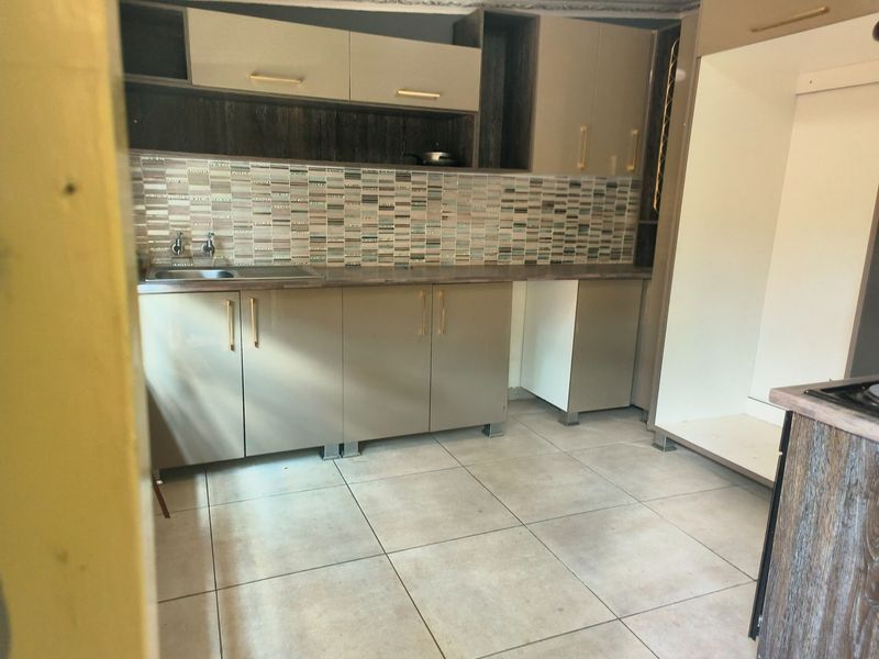 A clean, modern kitchen featuring neutral-toned cabinetry, a decorative mosaic tile backsplash, and durable ceramic floor tiles with ample space for appliances.