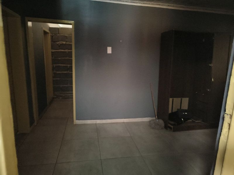 A dimly lit hallway featuring tiled flooring and access to an adjacent room with unfinished masonry walls.