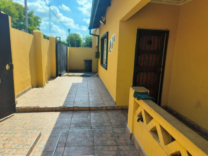 A view of the front entrance area featuring tiled flooring, a security gate, and a surrounding boundary wall.