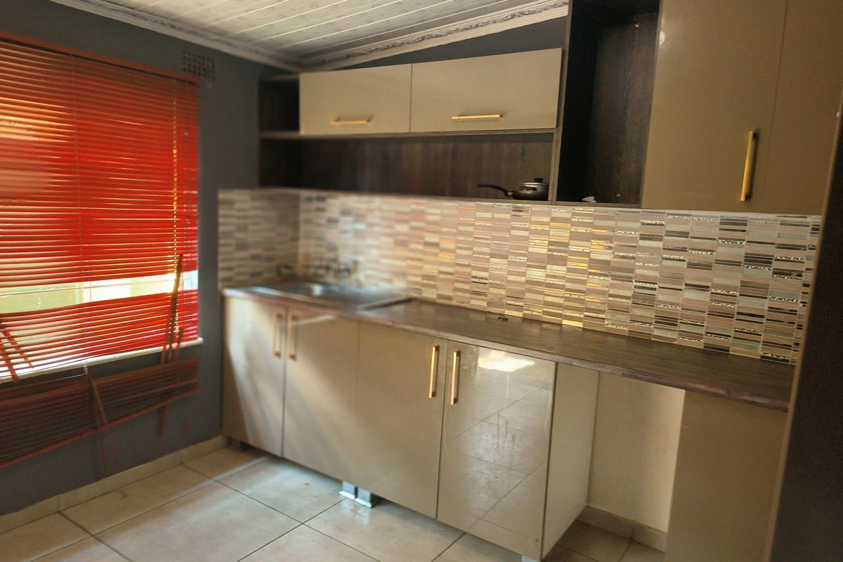A compact kitchen featuring modern high-gloss cabinetry, a mosaic tile backsplash, and neutral floor tiling, offering a functional prep space.