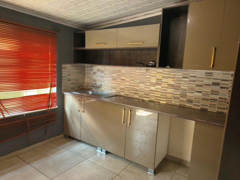 A compact kitchen featuring modern high-gloss cabinetry, a mosaic tile backsplash, and neutral floor tiling, offering a functional prep space.