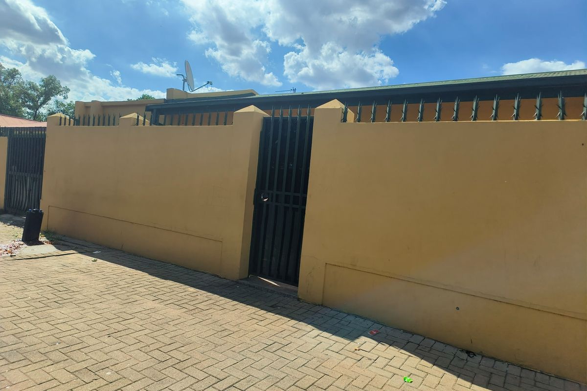 A secure street-facing perimeter wall featuring a metal pedestrian gate, security spikes, and a paved driveway area.