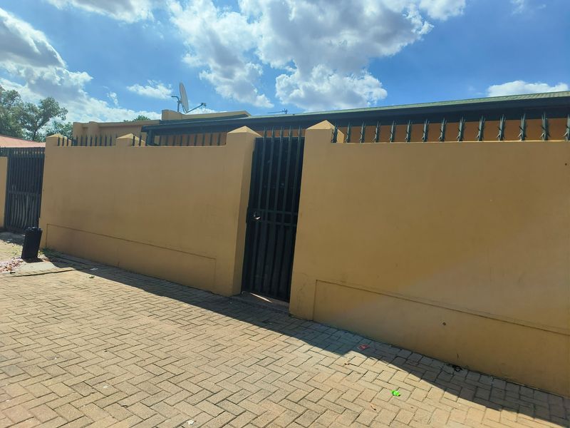 A secure street-facing perimeter wall featuring a metal pedestrian gate, security spikes, and a paved driveway area.