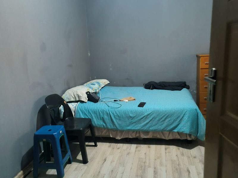 A bedroom featuring laminate flooring and grey walls showing signs of wear and scuffing.