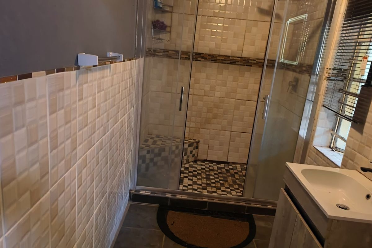 A functional bathroom featuring a glass-enclosed shower with a built-in bench, tiled walls, and a modern vanity basin.