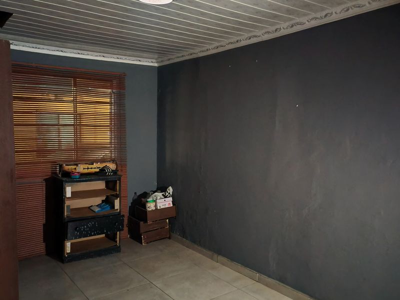A vacant bedroom featuring tiled flooring, a panelled ceiling with coving, and venetian blinds, presenting a blank canvas for renovation.