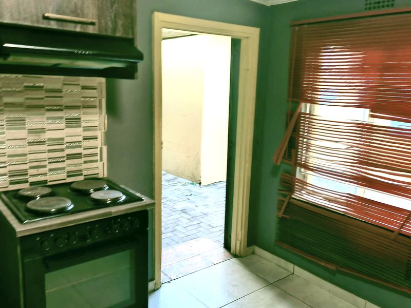 A compact kitchen area featuring a built-in oven, hob, extractor fan, and tiled backsplash, with direct access to an outdoor paved area.