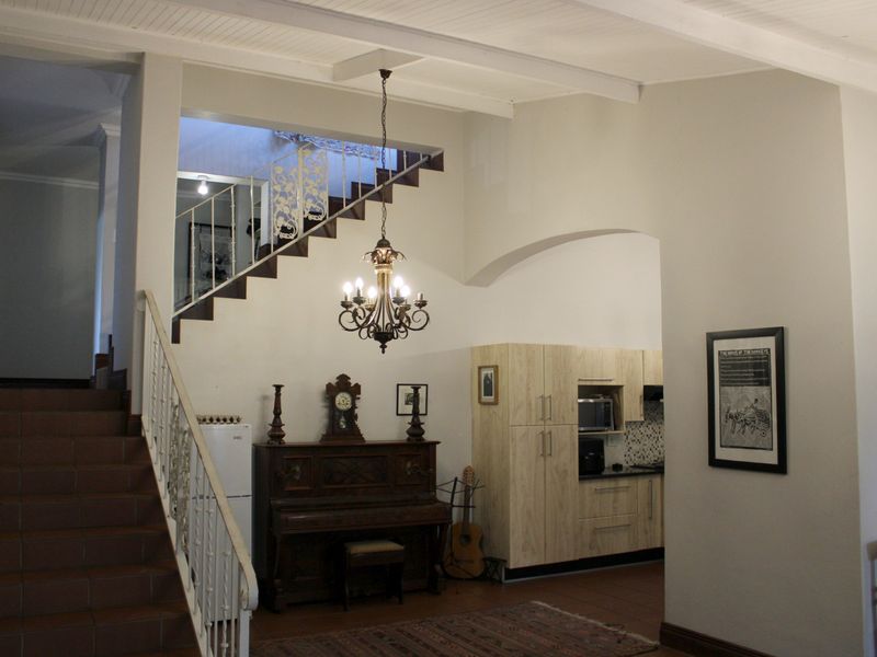 Open plan living area featuring a prominent staircase with wrought iron balustrade, exposed ceiling beams, and an integrated kitchen space with modern cabinetry.