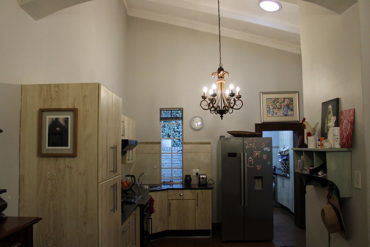 A functional kitchen featuring light wood-finish cabinetry, dark countertops, a vaulted ceiling, and a decorative chandelier, with an adjacent scullery area.