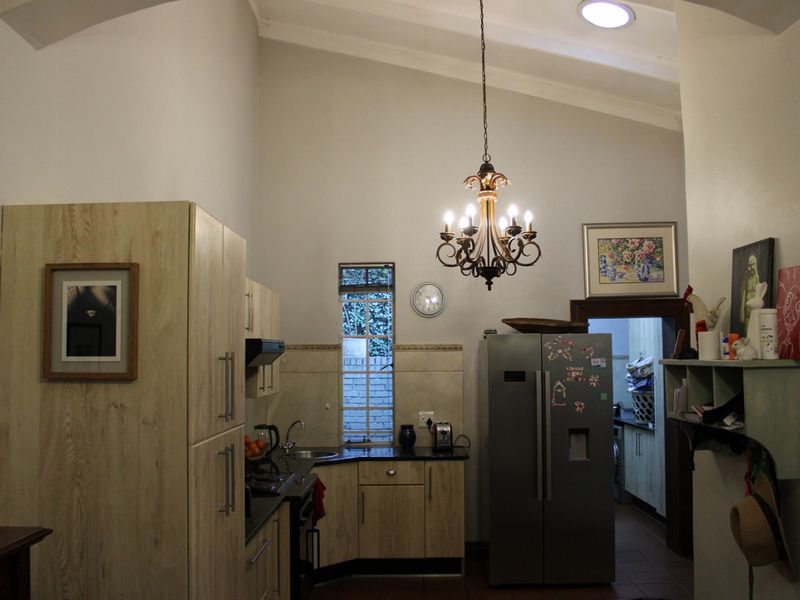 A functional kitchen featuring light wood-finish cabinetry, dark countertops, a vaulted ceiling, and a decorative chandelier, with an adjacent scullery area.