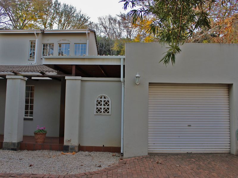 Front elevation of a two-story house featuring a garage, covered patio area, and brick driveway with mature trees in the background.