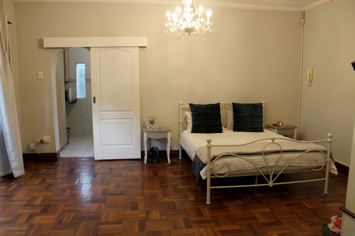 Spacious bedroom featuring classic parquet flooring, an elegant chandelier, and a sliding door leading to an adjoining space.