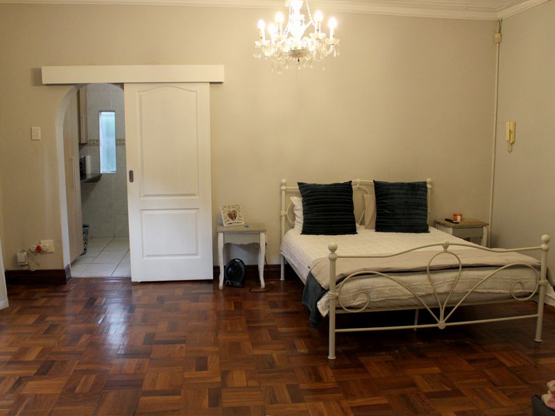 Spacious bedroom featuring classic parquet flooring, an elegant chandelier, and a sliding door leading to an adjoining space.