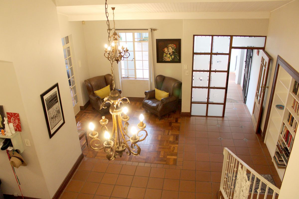 Spacious living area featuring a blend of parquet and terracotta tile flooring, a decorative chandelier, built-in shelving, and a unique frosted glass room divider.