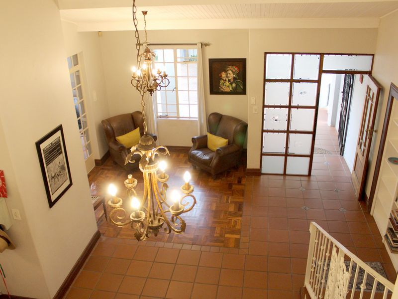 Spacious living area featuring a blend of parquet and terracotta tile flooring, a decorative chandelier, built-in shelving, and a unique frosted glass room divider.