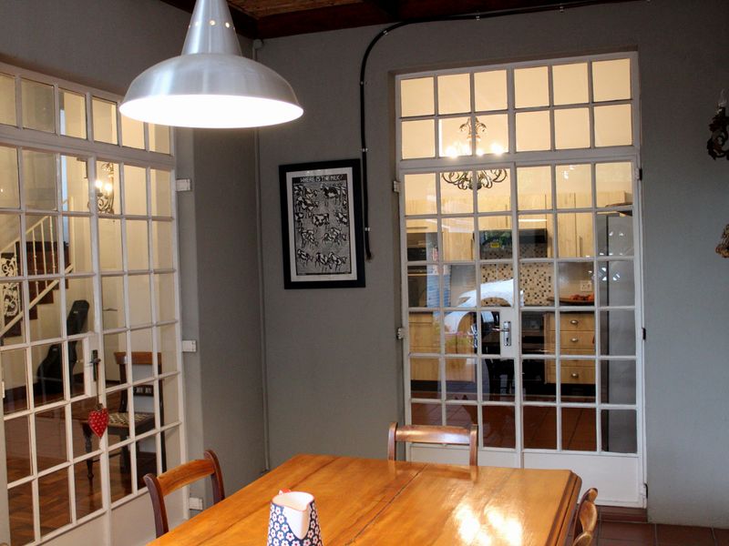 Dining area featuring classic French doors, exposed timber ceiling beams, and a modern pendant light, providing a view into the adjacent kitchen space.