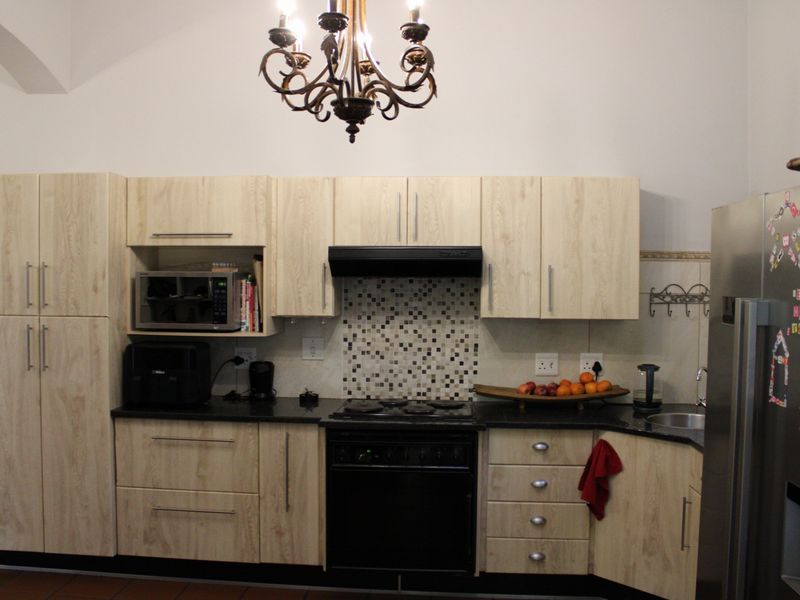 A functional kitchen featuring light-wood cabinetry, black granite countertops, a mosaic tile backsplash, and integrated cooking appliances.
