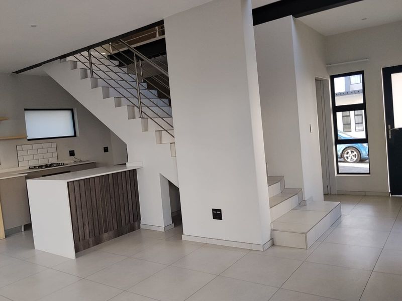 Modern open-plan living area featuring a sleek kitchen island, built-in hob, and a contemporary staircase with stainless steel balustrades.