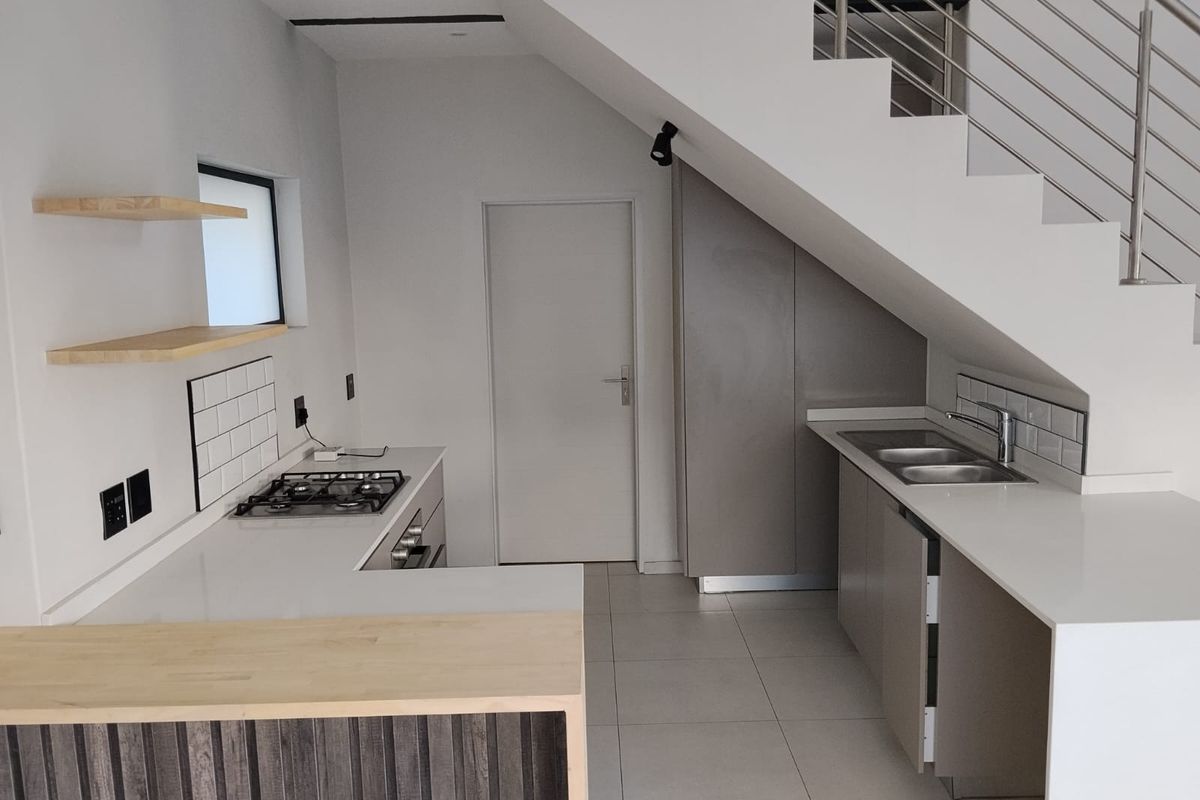 Modern kitchen featuring quartz countertops, gas hob, built-in oven, and subway tile backsplash, efficiently designed under the staircase.