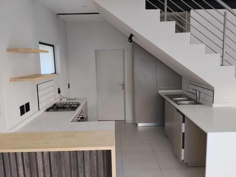 Modern kitchen featuring quartz countertops, gas hob, built-in oven, and subway tile backsplash, efficiently designed under the staircase.