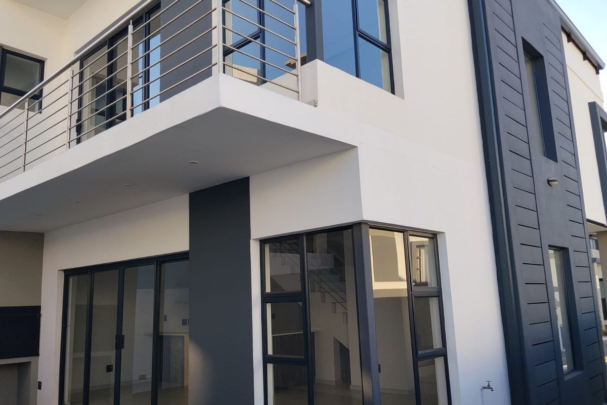 Modern townhouse exterior featuring a spacious balcony with stainless steel balustrades, large aluminium-framed windows, and sliding glass doors leading to the interior.