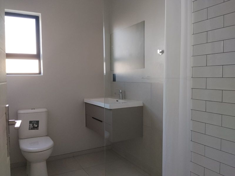Modern bathroom featuring a wall-mounted vanity, ceramic toilet, glass shower screen, and subway tile accents.