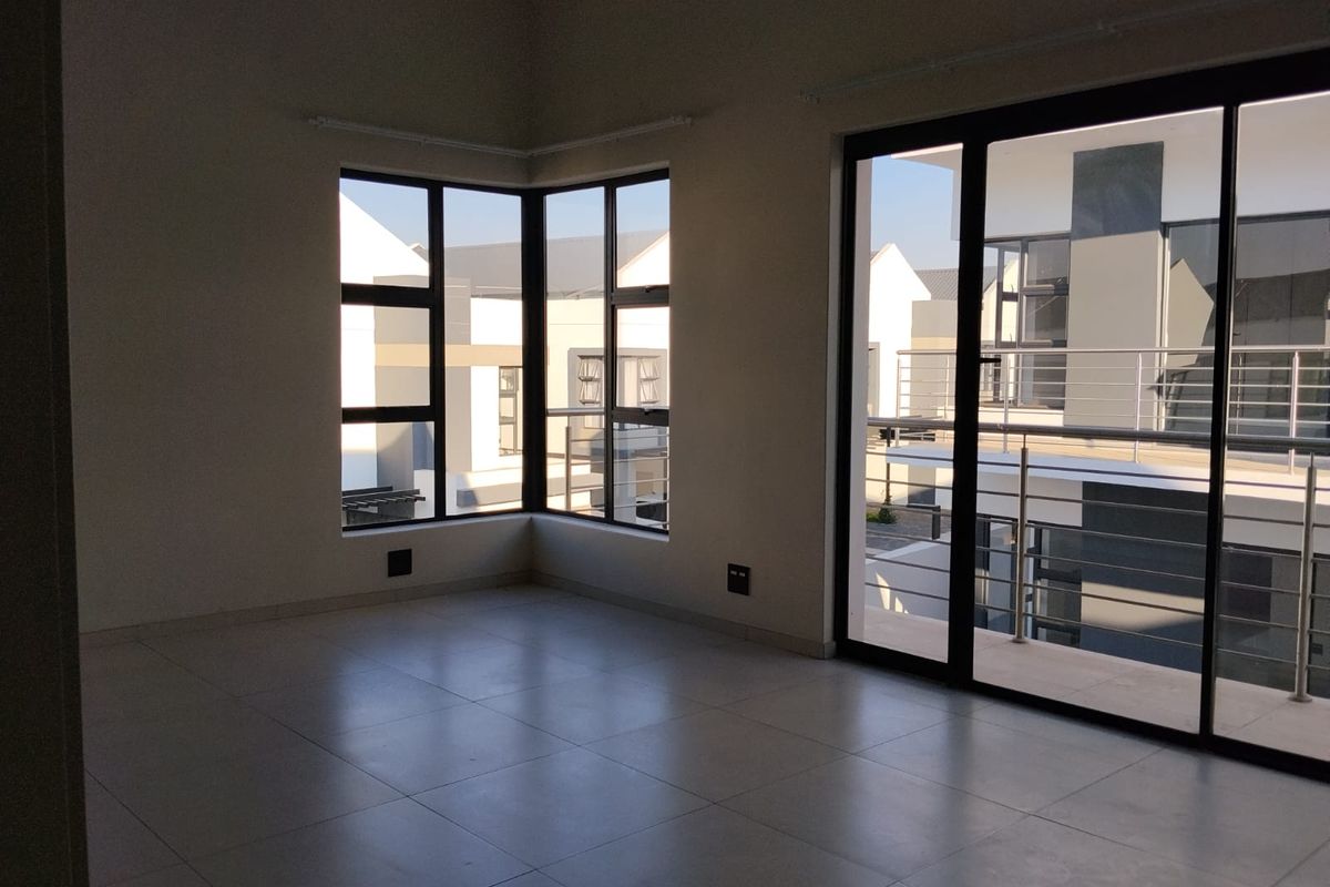 An empty, modern living area featuring large corner windows, tiled flooring, and sliding glass doors that open onto a balcony.