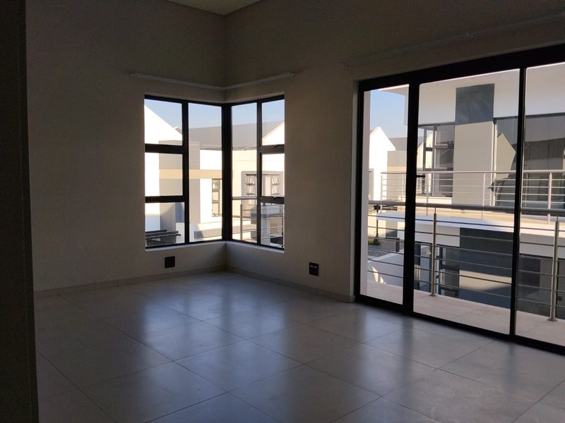An empty, modern living area featuring large corner windows, tiled flooring, and sliding glass doors that open onto a balcony.
