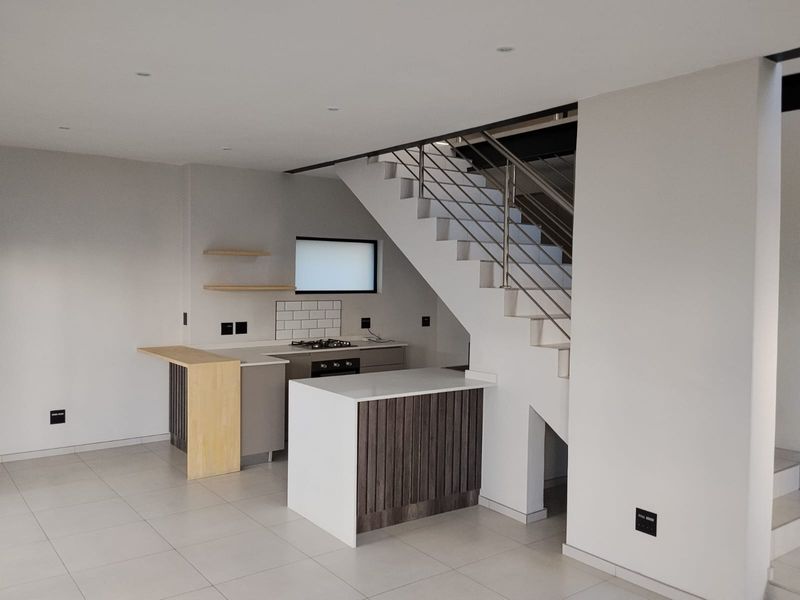 Modern open-plan kitchen area featuring sleek cabinetry, stone countertops, integrated appliances, and a contemporary staircase with stainless steel balustrades.