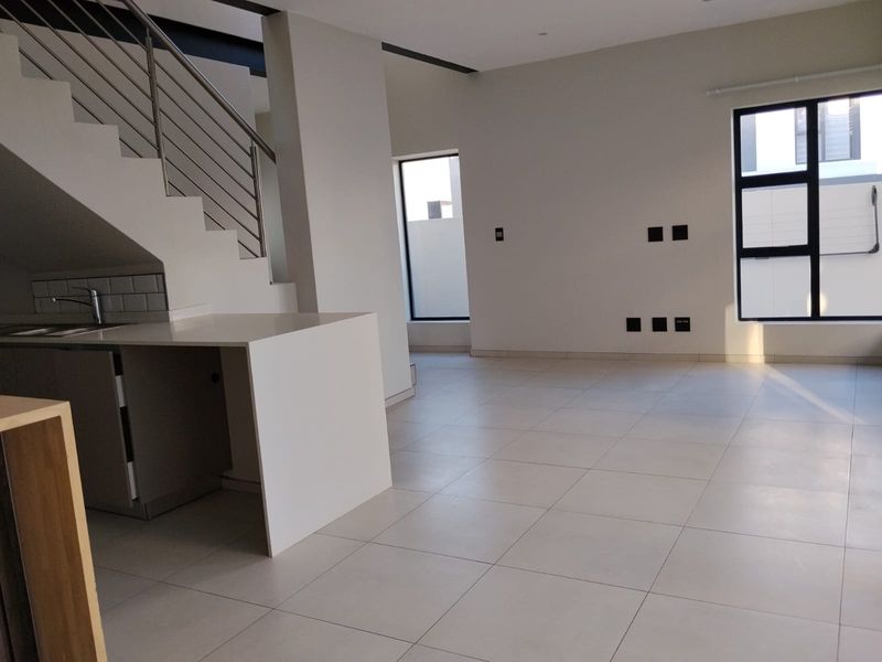 Spacious open-plan living area featuring modern tiled flooring, a sleek staircase with stainless steel balustrades, and a compact kitchen corner.