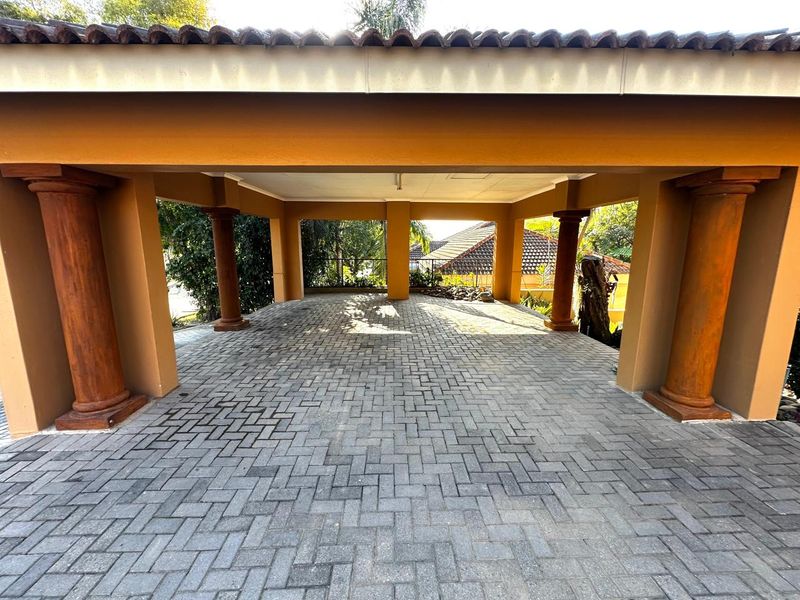 A spacious, covered carport featuring decorative columns and durable paved flooring, providing ample sheltered parking space.