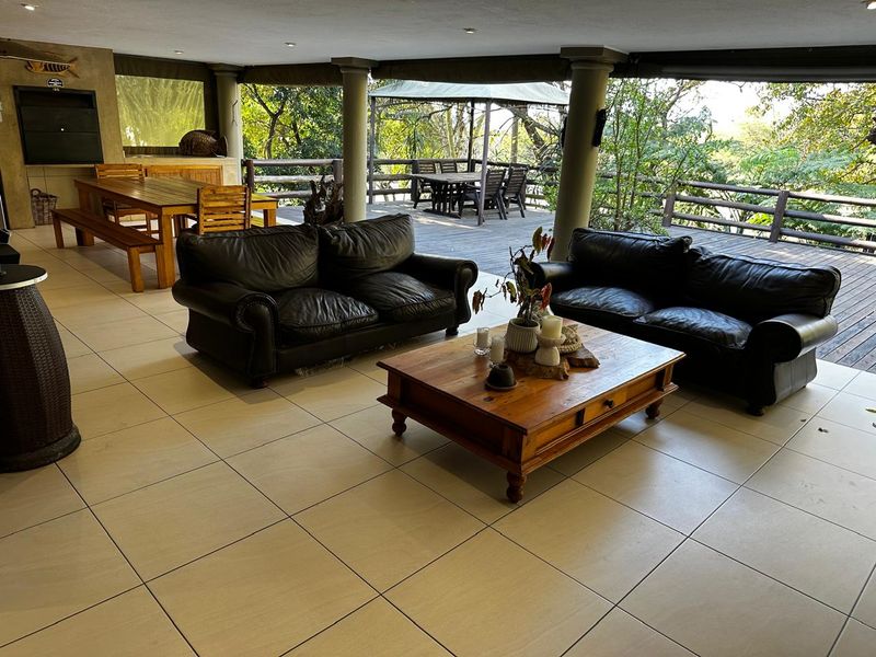 Spacious covered patio featuring tiled flooring, recessed lighting, and a built-in braai, seamlessly transitioning to an open wooden deck area overlooking the garden.