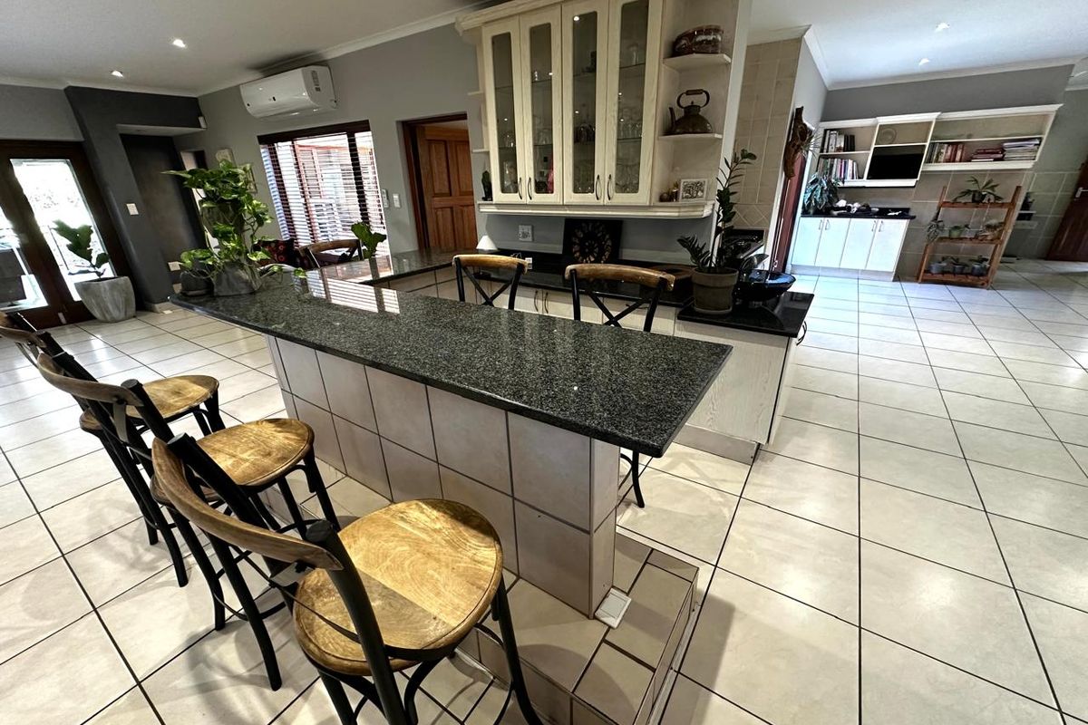 Spacious kitchen featuring a large granite-topped breakfast bar, custom glass-front cabinetry, and neutral ceramic floor tiles throughout the open-plan living area.