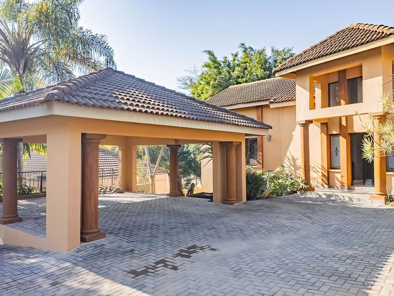 Front elevation of a residential property featuring a paved driveway, a spacious covered carport with decorative columns, and a well-maintained stucco facade.